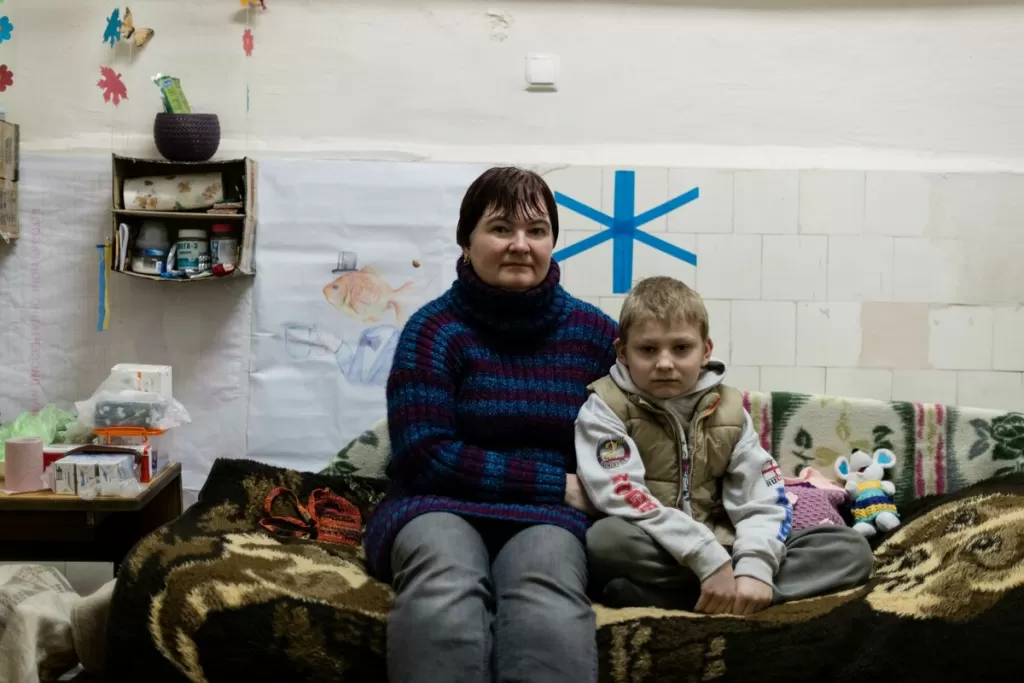 Yulia and her son, Kolia* sit on a bed in a public bomb shelter in Kharkiv.
