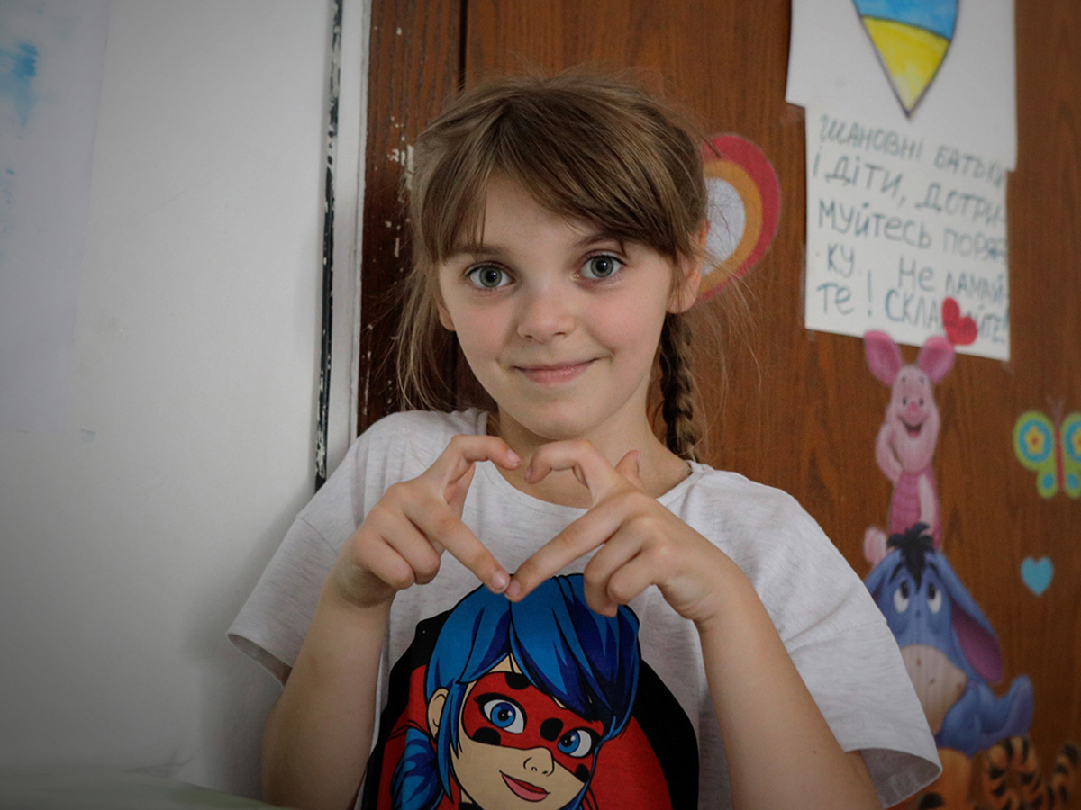 A girl who is a refugee from Ukraine makes a heart sign