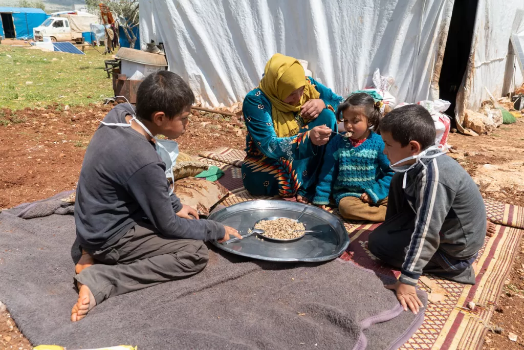 A family share a meal in a camp for displaced people in Idlib province, Syria. A food crisis also looms in the country.