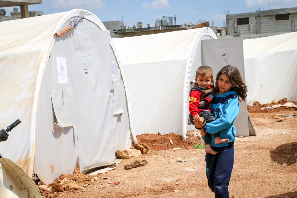 Laia* and Nasir* walk past tents in the camp for displaced people where they live.