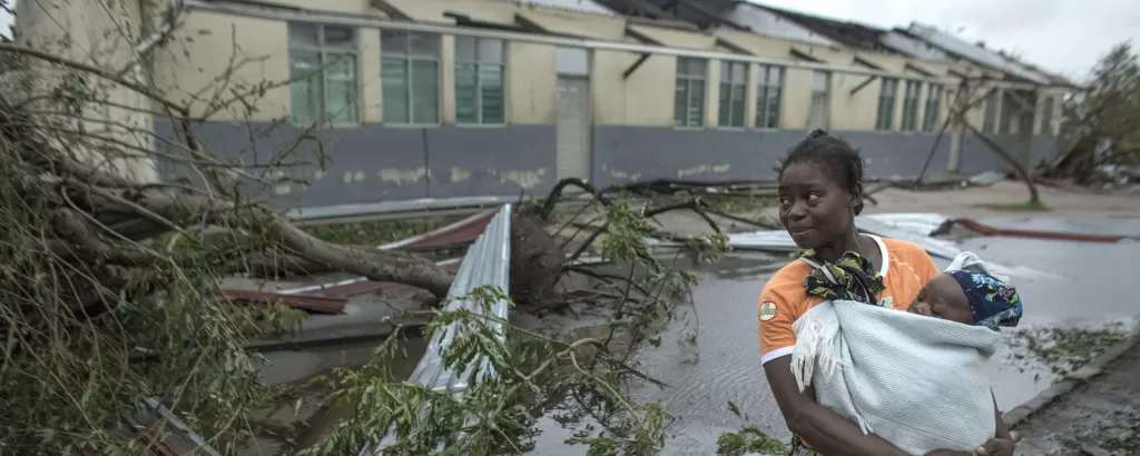 A woman holds a baby by a fallen tree after Cyclone Idai