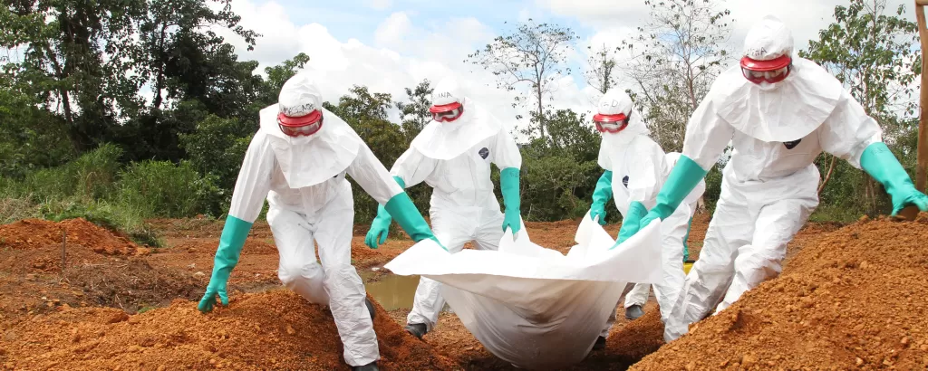 Aid workers in PPE carry a body bag to a grave