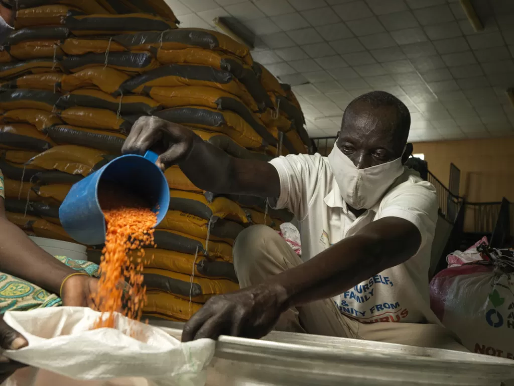An aid worker pours lentils into a sack