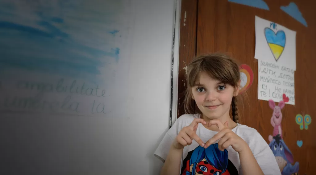 A girl who is a refugee from Ukraine makes a heart sign