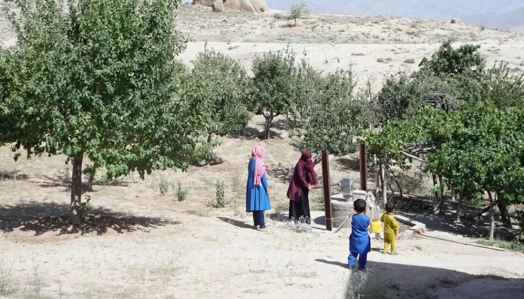 Aina*, a 30 year-old mother and beneficiary of a cash distribution programme, pumps water with her hands while her children play around her in Daykundi Province, Afghanistan on 28 May 2022.