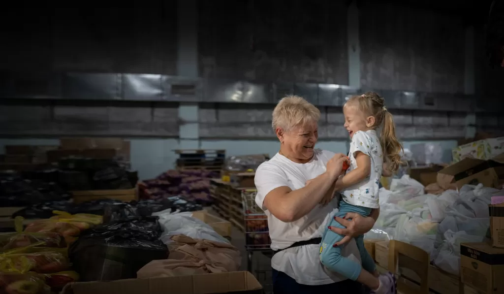 Woman holding and tickling a child in a food storage warehouse, both are laughing
