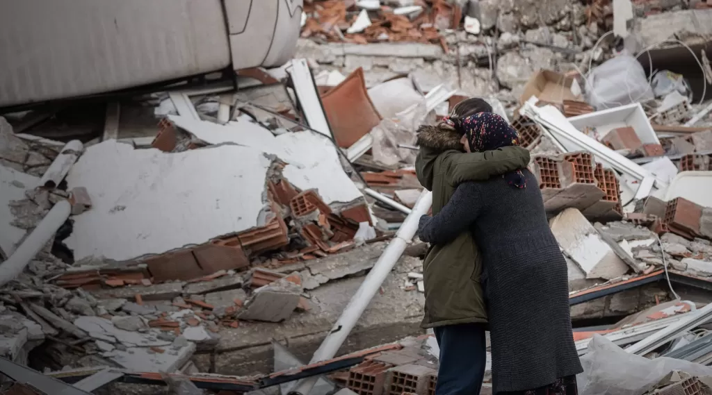 Women hug each other near a collapsed building in Hatay, Turkey following the devastating earthquakes in February 2023. 