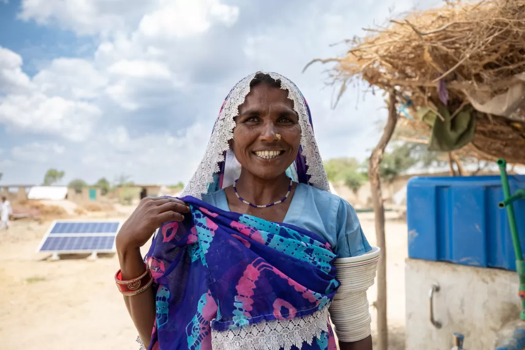 Lakshmi stand in front of a solar water supply system installed by DEC member International Rescue Committee.