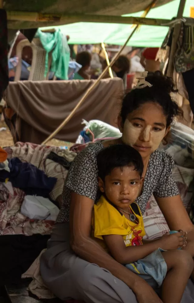 A mother sits on the ground ith her child in her lap in a makeshift shelter