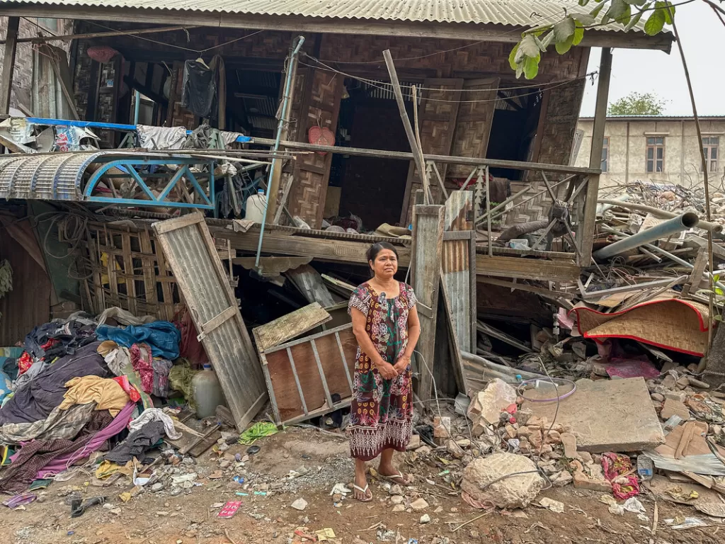 Women stands in front of collapsed house 