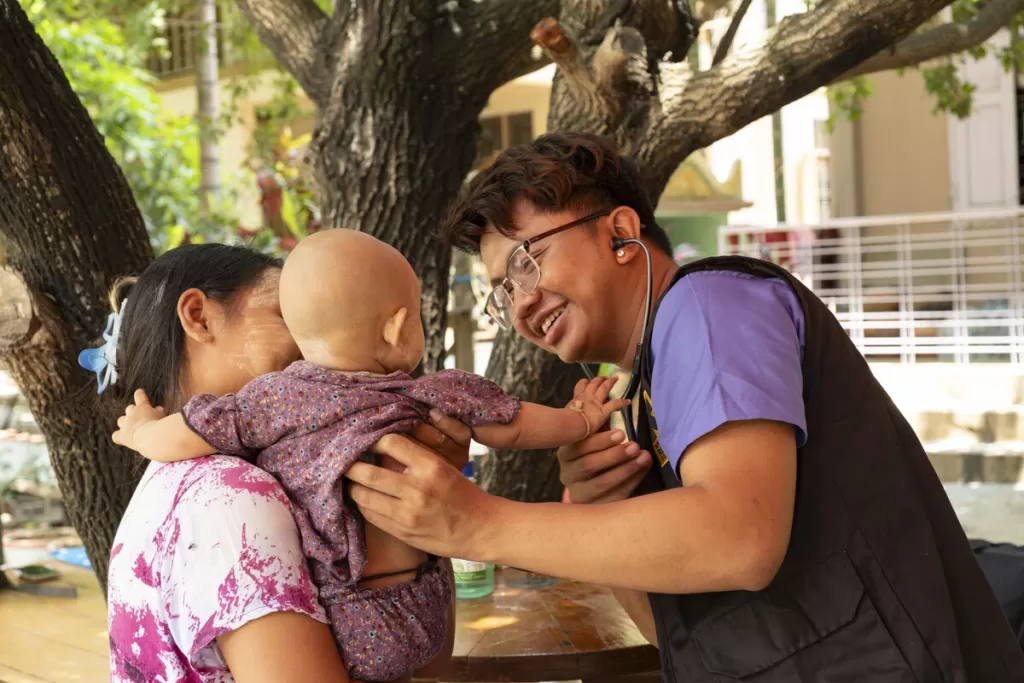 Doctor hugs baby in mothers arms in Myanmar