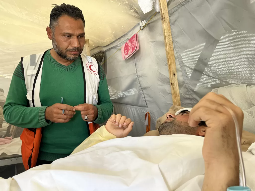 A medical worker wearining ICRC branded jacket attends a patient lying on a hospital bed whose face is not clearly visible