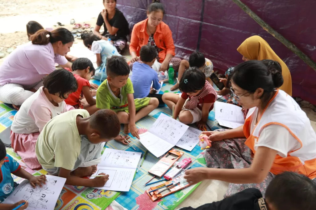 Children in Myanmar do colouring sat on a blanket with World Vision