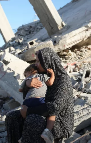 Aaliyah* holds her daughter on the remains of a damaged building in Gaza in October 2024. The mother of six built a temporary shelter opposite her demolished house and depends entirely on aid to feed her family. Photo: DEC/Arete/Abdallah Alsayed