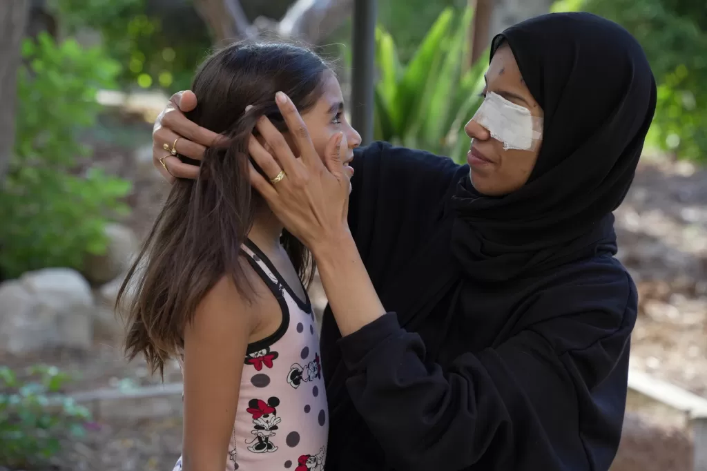 Woman in hijab with bandaged nose gently holding the face of a young girl in a polka dot dress outdoors