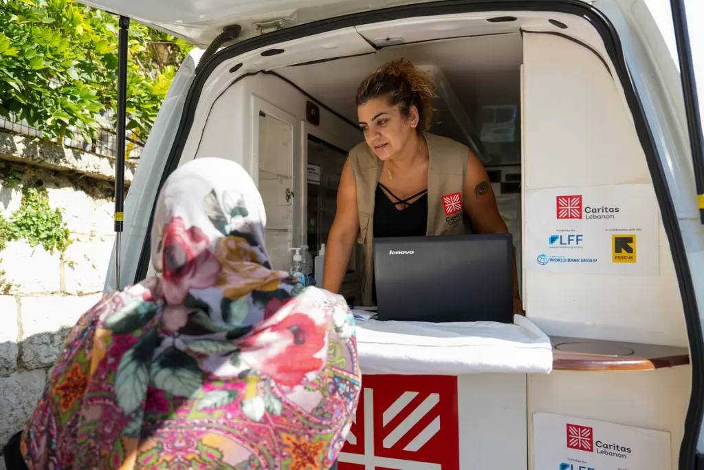 Aid worker in a mobile unit speaks with a woman wearing a floral headscarf