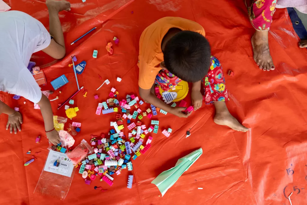 Children playing with colorful building blocks and toys scattered on a red tarp during an outdoor activity session