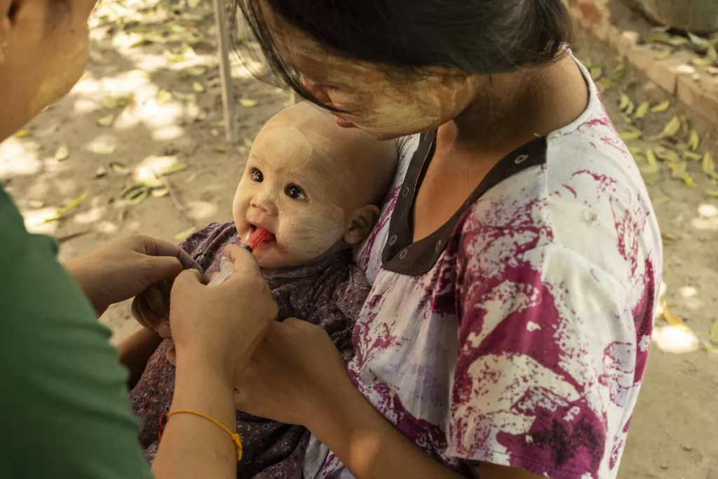 Woman holding infant who is being given oral medication outdoors in a medical care setting