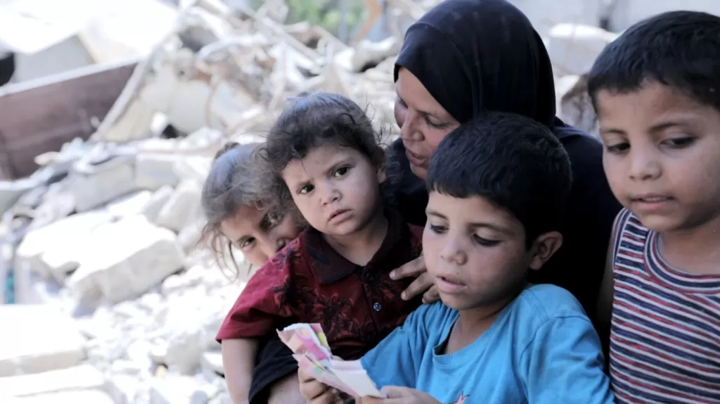 Nedaa*, 40, sits with her children (L-R) Amera* (12), Aseel* (2), Ahmed (9) and Hamed (7), outside the tent they now live in on the site of their destroyed home in Gaza, 28 July 2025.