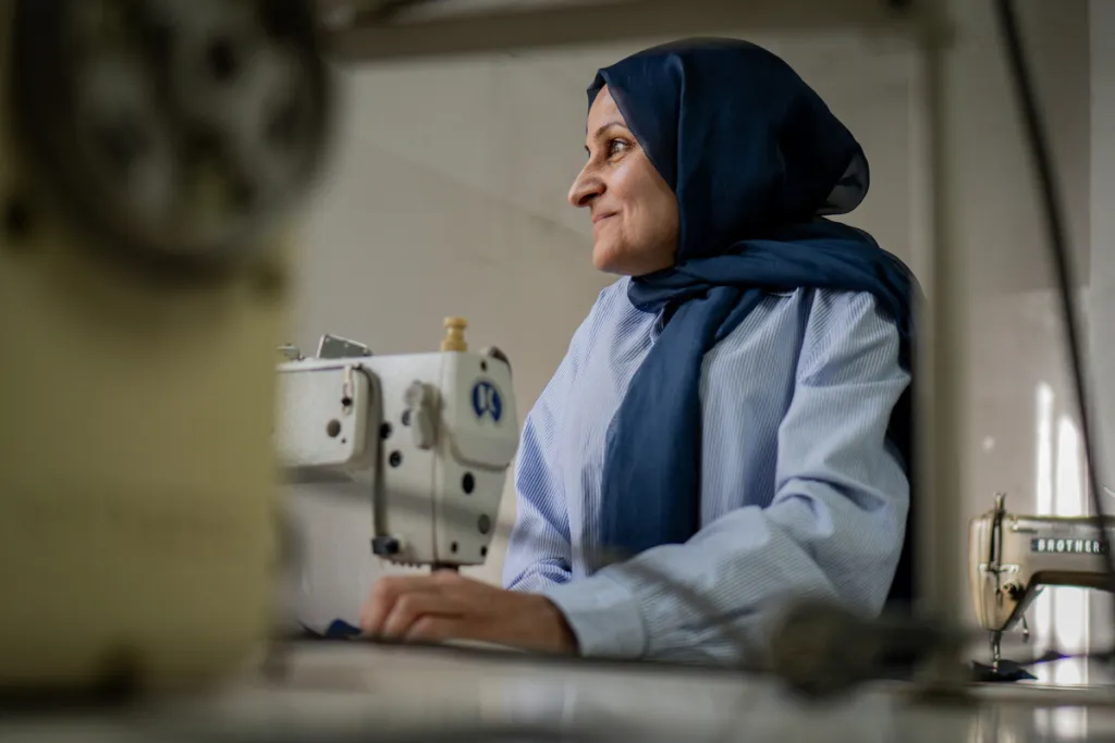 Older women in headscarf sits by sewing machine in Lebanon, slightly smiling 