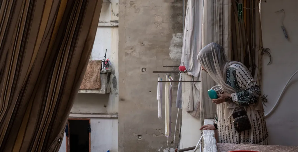 A woman peers over the balcony, her face obscured by a scarf