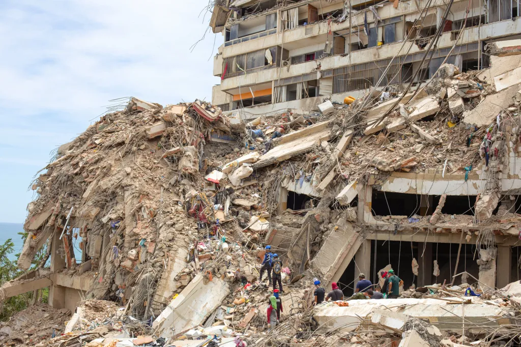 Large scale destruction with a partially destroyed building with rescue workers on the rubble