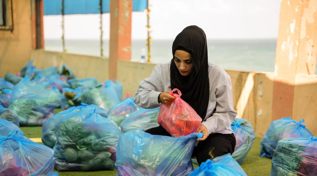 A woman crouches among bags of fresh fruit and vegetables collecting food items