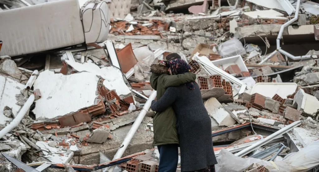 Women hug near a collapsed building in Turkey after one loses her brother in the devastating earthquake in February 2023. 