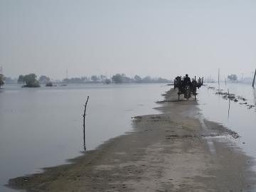 People travel along a road between flooded fields