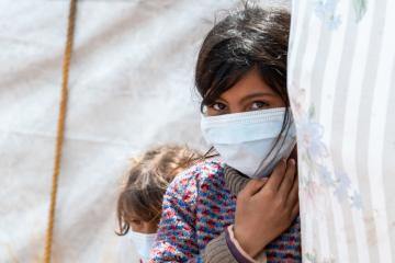 A girl wearing a mask peers round a tent