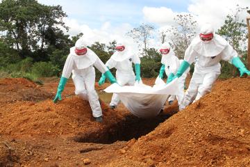 Aid workers in PPE carry a body bag to a grave