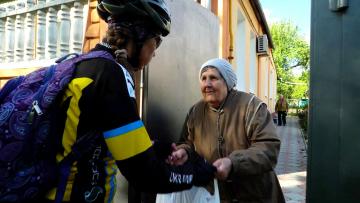 Cyclist hands a bag of food to an older lady