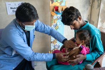 Nutrition officer, Mehbood Ali, physically examines severely malnourished Saba* with her father Nadeem at a medical camp organised for flood affected communities
