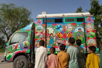 Children look on as a truck painted in traditional Pakistani truck art style traverses a village that was previously submerged in the floods in Pakistan