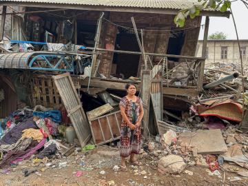 Women stands in front of collapsed house 