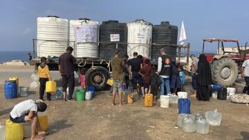 People queue with jerry cans before a truck that carries five large cylinders of water