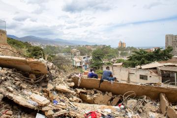 The backs of two people sitting on a vast landscape of rubble and destruction