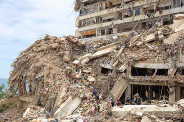 Large scale destruction with a partially destroyed building with rescue workers on the rubble