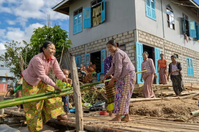 Women work together to move bamboo material for house construction