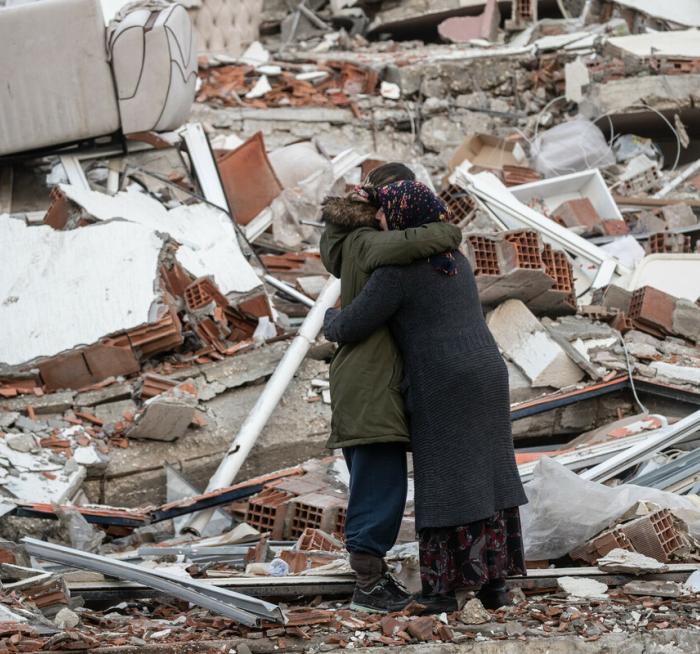 Women hug near a collapsed building in Turkey after one loses her brother in the devastating earthquake in February 2023.